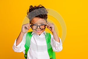 Portrait of toothy beaming smart boy with backpack wear stylish shirt touching glasses toothy smiling isolated on yellow