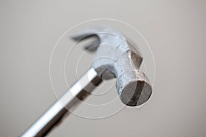 A portrait of the top part of a metal claw hammer isolated on a grey background. The tool is a bit worn by using it for work in