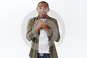 Portrait of touched, happy african-american man sighing and touching heart as hear pleasant news, look at adorable photo