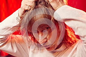 Portrait of tousled disheveled middle-aged woman looking like a madwoman on red background in studio. Actress during the