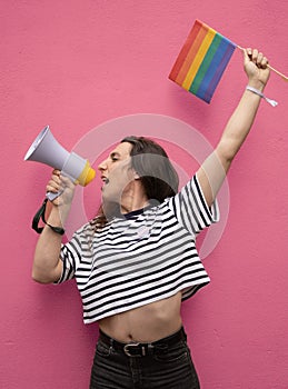 Portrait of transgender woman shouting with a megaphone and holding a rainbow flag supporting LGBTQ community