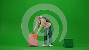 Portrait of traveler isolated on chroma key green screen background. Young girl puts heavy suitcase on the ground takes