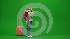 Portrait of traveler isolated on chroma key green screen background. Young girl with suitcase standing taking pictures