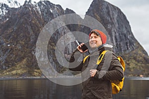 Portrait traveler man talking on mobile phone. Tourist in a yellow backpack standing on a background of a mountain and a