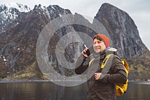 Portrait traveler man talking on mobile phone. Tourist in a yellow backpack standing on a background of a mountain and a lake.