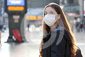 Portrait of traveler woman wearing surgical mask at train station looking worried in front of her. Copy space