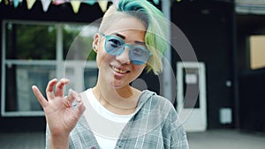 Portrait of trendy Asian girl showing OK hand gesture and smiling outdoors