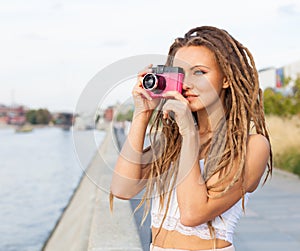 Portrait of Trendy Girl with Dreads and Vintage Camera Standing by the River. Modern Youth Lifestyle Concept. Take the picture.