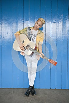 Portrait of a trendy teenage boy playing guitar against wood paneled wall