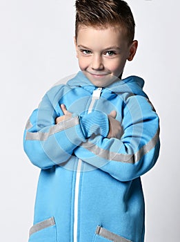Portrait of tricky smiling kid boy in blue jumpsuit with hood standing holding arms crossed at chest
