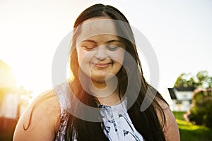 A Portrait of trisomie 21 adult girl outside at sunset