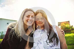 A Portrait of trisomie 21 adult girl smilin outside at sunset with family friend