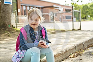 A portrait of trisomie 21 child girl outside on a school playground