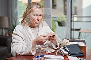 Portrait of troubled ill mature woman sitting at home and reading discription of medication in her hand.