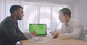 Portrait of two adult successful businessmen having a formal discussion with laptop with green chroma screen in the