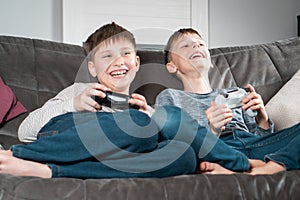 Portrait of two amazing barefoot teenage boys children sitting at home, holding gaming controller, playing videogames.