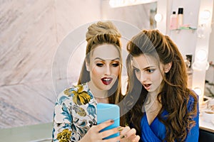 Portrait two astonished pretty women looking at phone in beauty salon. Having fun, gossip girls, preparing to party