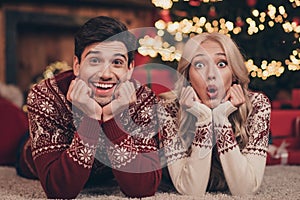 Portrait of two attractive amazed married spouses lying on carpet holly jolly sudden news reaction spending day December