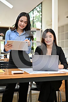 Portrait, Two attractive Asian businesswomen working together, using laptop and tablet