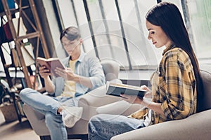 Portrait of two attractive cheerful focused people sitting in chair reading interesting book at loft industrial interior