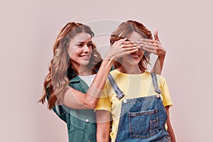 Portrait of two attractive twin sisters in casual wear. Young girl covering sisters eyes with hands to surprise her