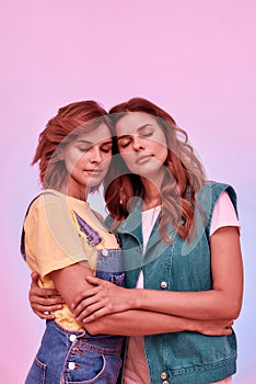 Portrait of two attractive young girls, twin sisters holding each other, posing together with eyes closed  over