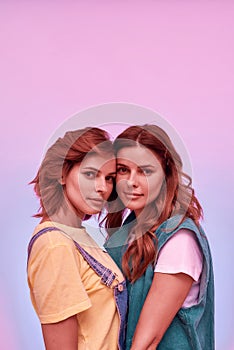 Portrait of two attractive young girls, twin sisters looking at camera, posing together  over pink background