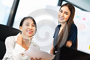 Portrait of two beautiful Asian office coworkers smiling together at work. Business colleagues, teamwork partner, job consultant