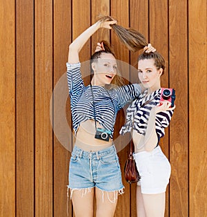Portrait of two beautiful fashionable girlfriends in denim shorts and striped t-shirt posing. Girl holding her by the hair.