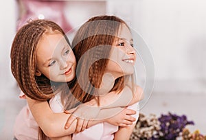 Portrait of two beautiful happy girls in a light room, cuddling and laughing