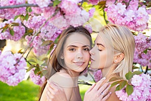 Portrait of a two beautiful spring girls. Two young women relaxing in sakura flowers. Lesbian couple kissing. Sensual