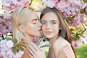 Portrait of a two beautiful spring girls. Two young women relaxing in sakura flowers. Lesbian couple kissing. Sensual