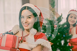 Portrait two beautiful woman holding gift box in hand and wearing red Santa Claus outfit and smiling happily, concept Christmas