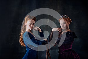 Portrait of two beautiful women in image of queen and princess isolated over dark background. Royal family