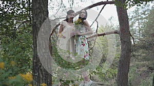 Portrait two beautiful women in short dresses standing on rocky ground with wild flowers and looking forest enjoying