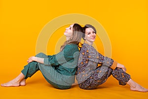 Portrait of two beautiful young girls wearing colorful pyjamas having fun during sleepover isolated over yellow