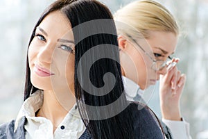 Portrait of two beautiful young women brunette & blond co-workers near office window at daytime