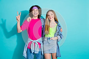 Portrait of two best friends youngster curly hair guy and blonde lady show v sign victory symbol isolated on aquamarine