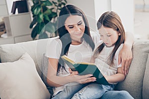Portrait of two brown haired people lovely caring mother teach her daughter read book girl concentrated sit divan couch