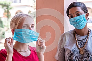 Portrait of two Caucasian and African girls in protective masks, coronavirus concept. teen girl removes medical mask.