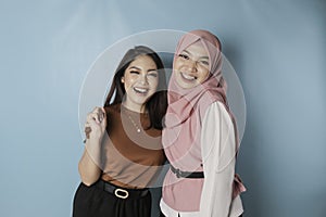 Portrait of two cheerful Asian women standing and laughing, isolated on blue background