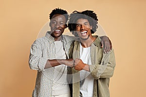 Portrait Of Two Cheerful Black Guys Embracing And Making Fist Bump Gesture