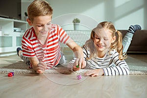 Portrait of two cheerful children laying on the floor and playing with colorful dices