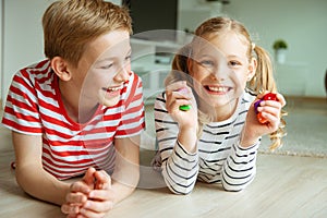 Portrait of two cheerful children laying on the floor and playing with colorful dices