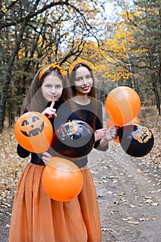 Portrait of two cheerful girls with black and orange balloons in the Halloween style
