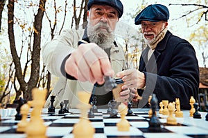 Portrait of two concentrated senior men playing chess in the park on a daytime in fall. Concept of leisure activity, old