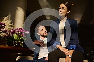 Portrait of two confident people, colleagues on business trip, Caucasian woman and man , business partners sitting on armchair in