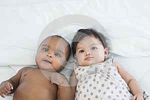 Portrait of two cute adorable smiling baby girl boy, three and four months old, lying on bed looking at camera. Top view. Diverse