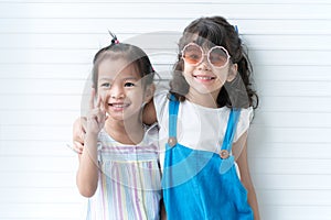 Portrait of two cute Asian and Caucasian little girls as friends hug each other, smiling, posing in studio white background.