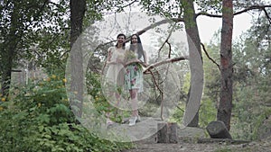 Portrait two cute beautiful women in short summer dresses standing on rocky ground with wild flowers and looking forest